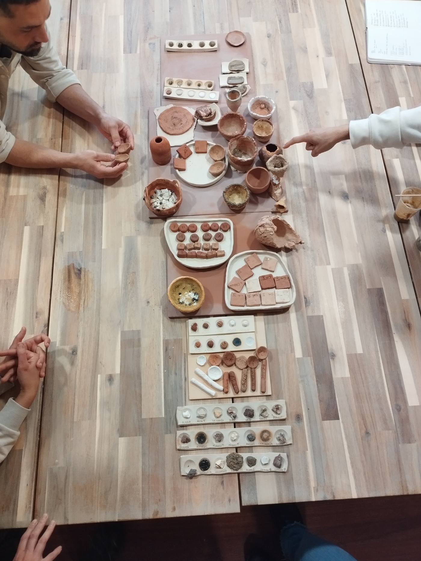 Mesa con decenas de muestras de pasta cerámica, cuencos y probetas de ensayo organizadas para su estudio.