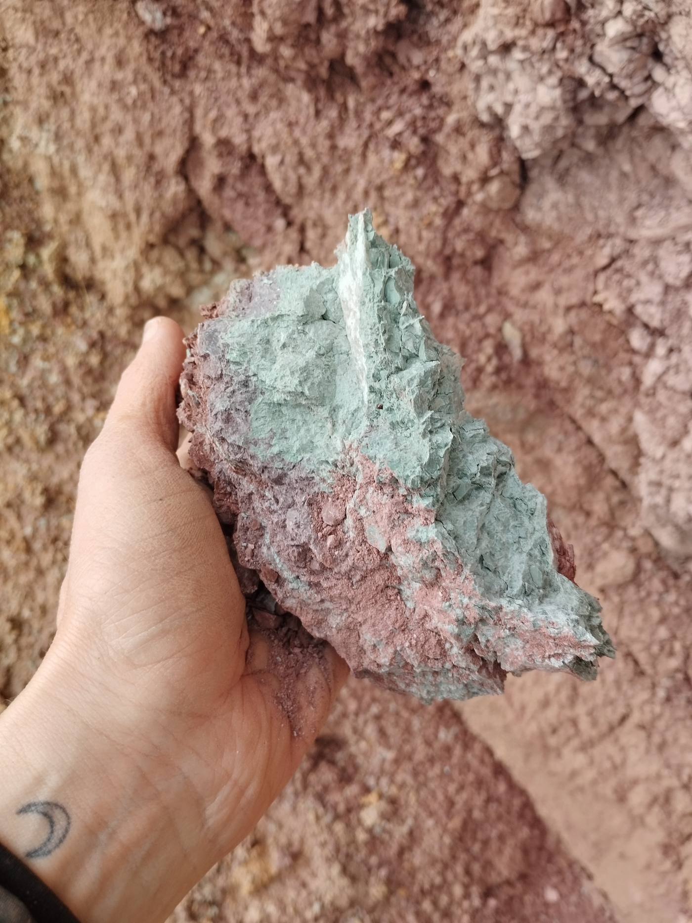 Fragmento de roca arcillosa sostenido frente a una pared de tierra.